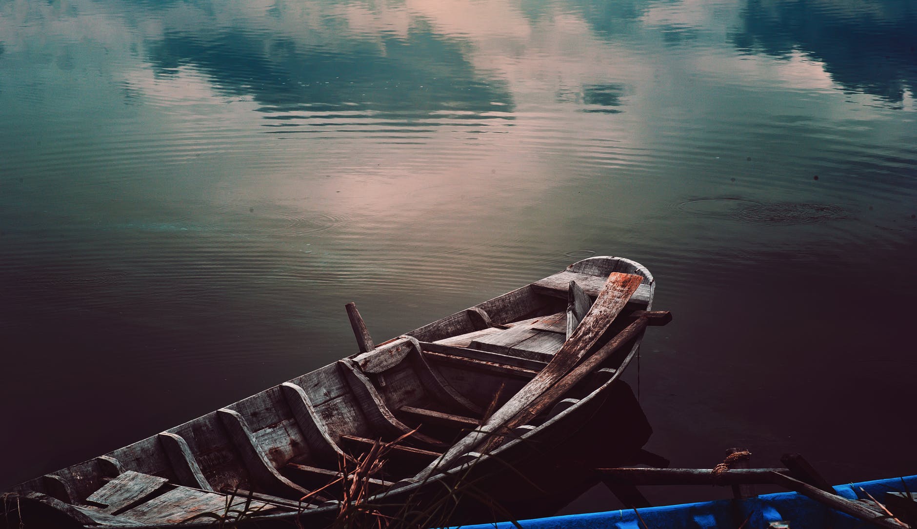 Image Description: A dreamy image of an old rowboat on a still lake. Clouds are mirrored in the water of the lake.