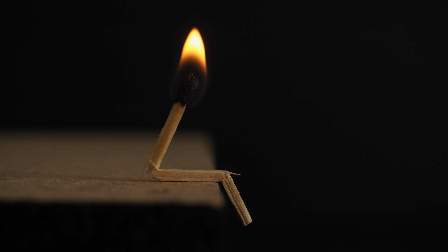 Image Description: A broken match is lit and sits at the edge of a table.