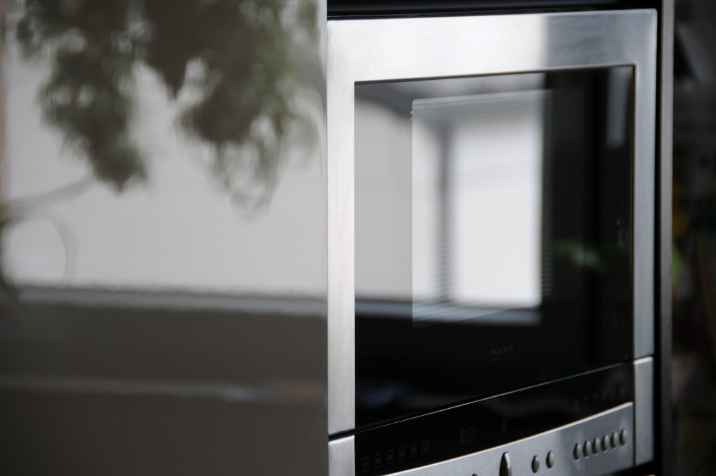 Chrome microwave reflects sunlit window and a tree branch.