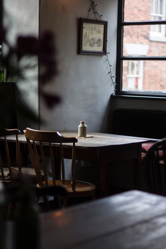 Photo of a table with two chairs by a window with a blur of shadow on the gray-plaster wall