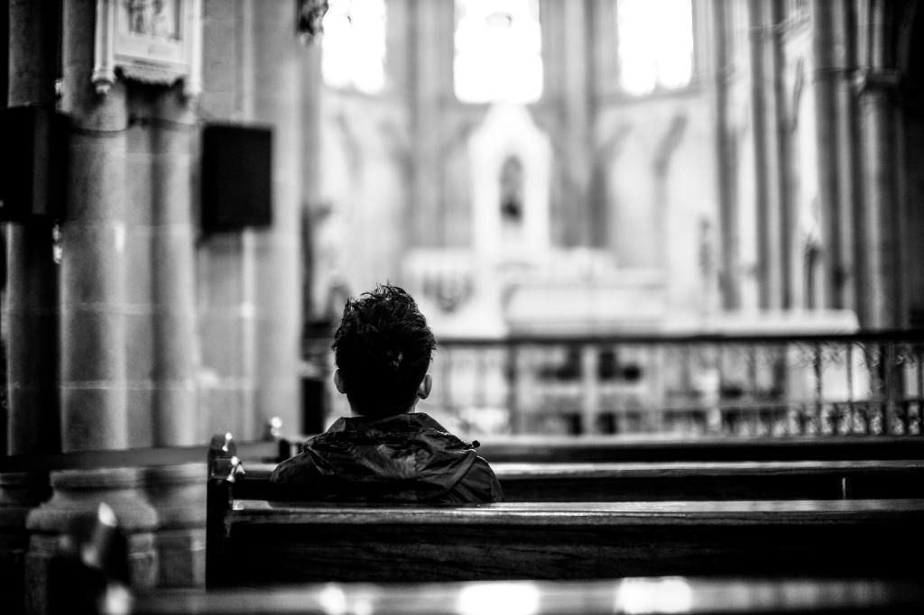 View from behind of a person with short hair and a jacket sitting in a church pew.