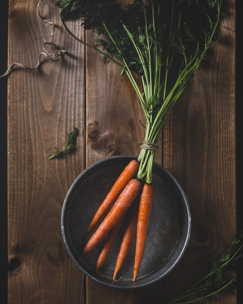 Carrots with long green stems in a bowl on a table