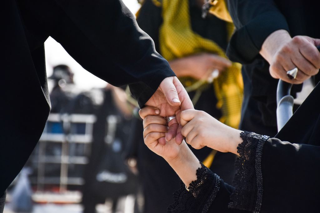 Close up of a child holding an adult's hand in a crowd of funeral goers. 