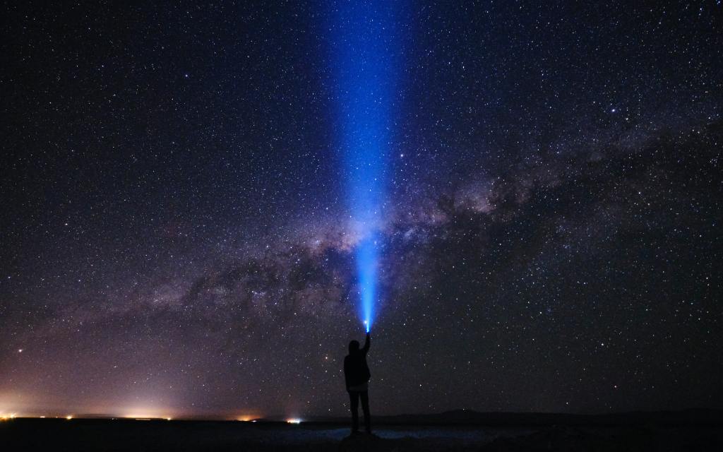 Descriptive image of silhouette of a person shining a flashlight into space.