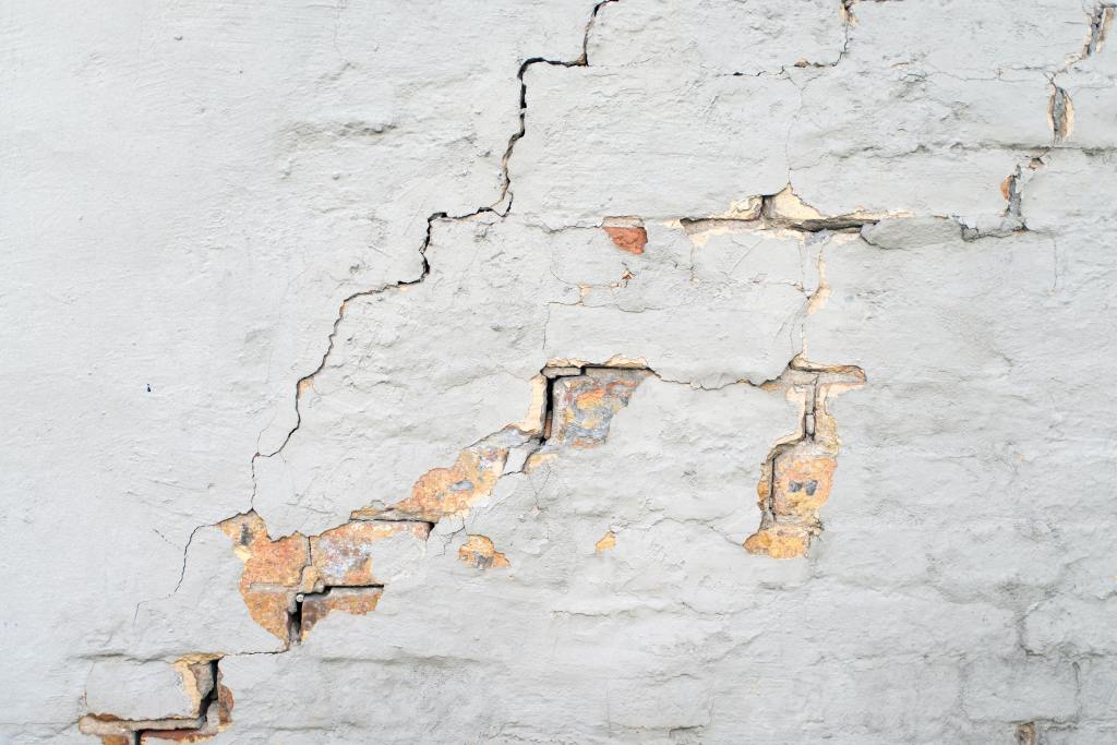 Cracks in drywall, exposing the bricks beneath on the wall. 